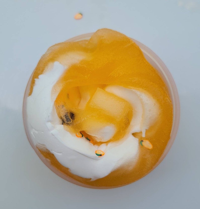 K&ouml;nnte beinhalten: Nahaufnahme eines durchsichtigen Beh&auml;lters, gef&uuml;llt mit einem Wirbel aus gelbem und wei&szlig;em Schleim mit orangefarbenem und gr&uuml;nem Glitzer.