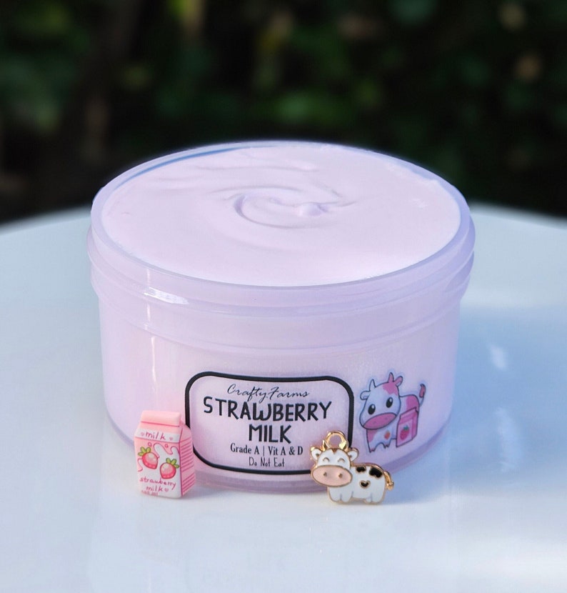 K&ouml;nnte beinhalten: Ein durchsichtiger Plastikbeh&auml;lter gef&uuml;llt mit rosa Erdbeermilch-Slime. Der Beh&auml;lter tr&auml;gt ein Etikett mit der Aufschrift "Crafty Farms Strawberry Milk" mit einer Comic-Kuh und einem kleinen Karton Erdbeermilch.