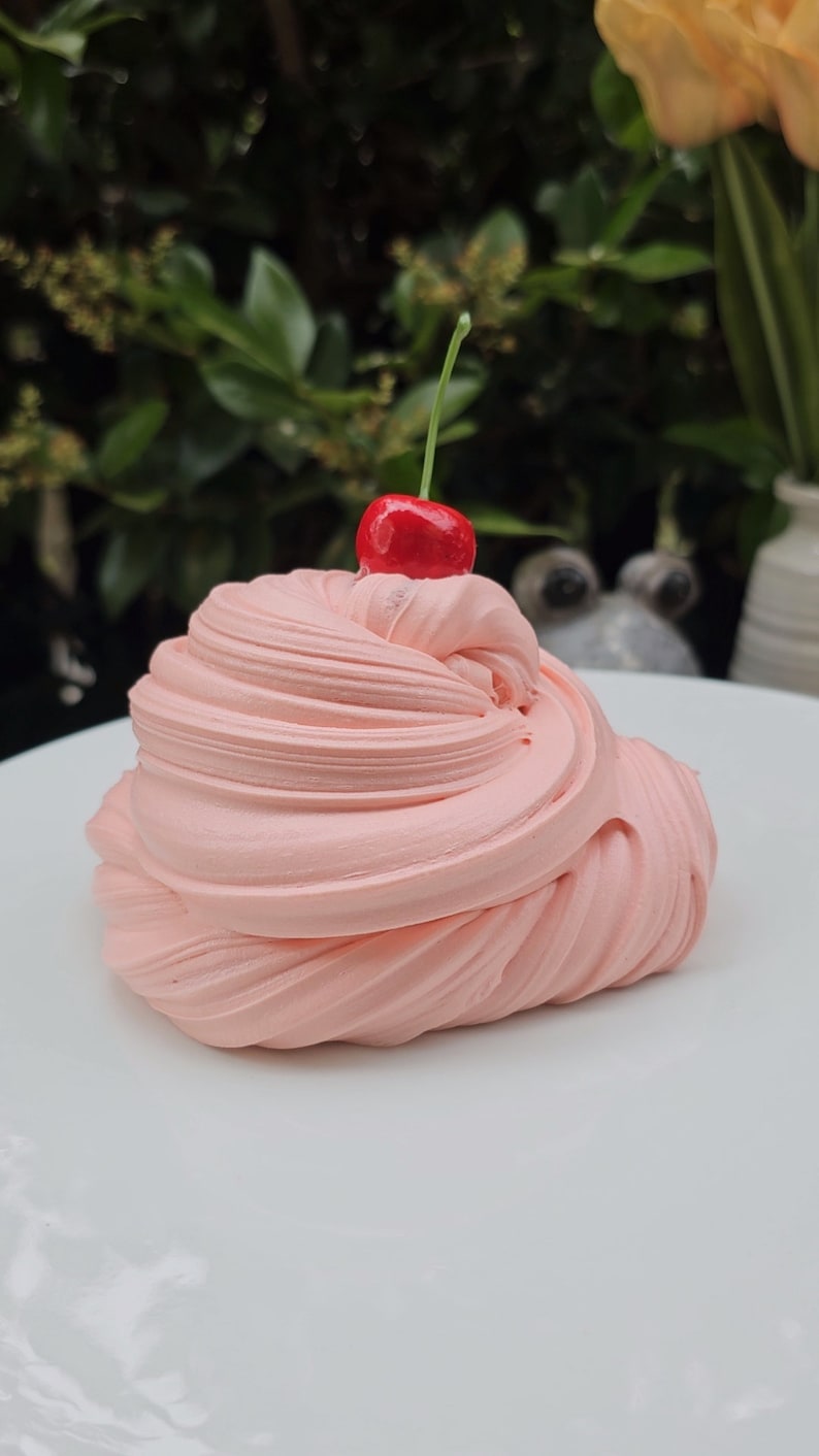 May include: A pink slime with a red cherry on top, sitting on a white plate.