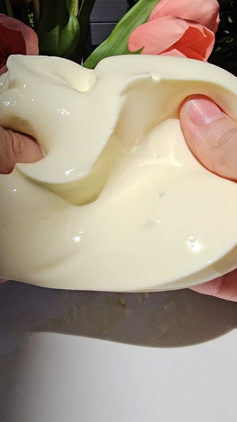 May include: A close-up of a white, creamy substance being stretched and pulled by a hand. The substance is smooth and glossy, with a slightly textured surface.