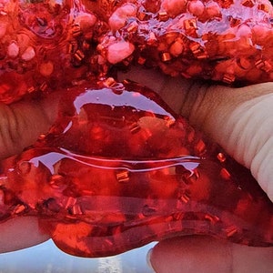 May include: Red slime with red glitter, held in a hand. The slime is very thick and gooey.
