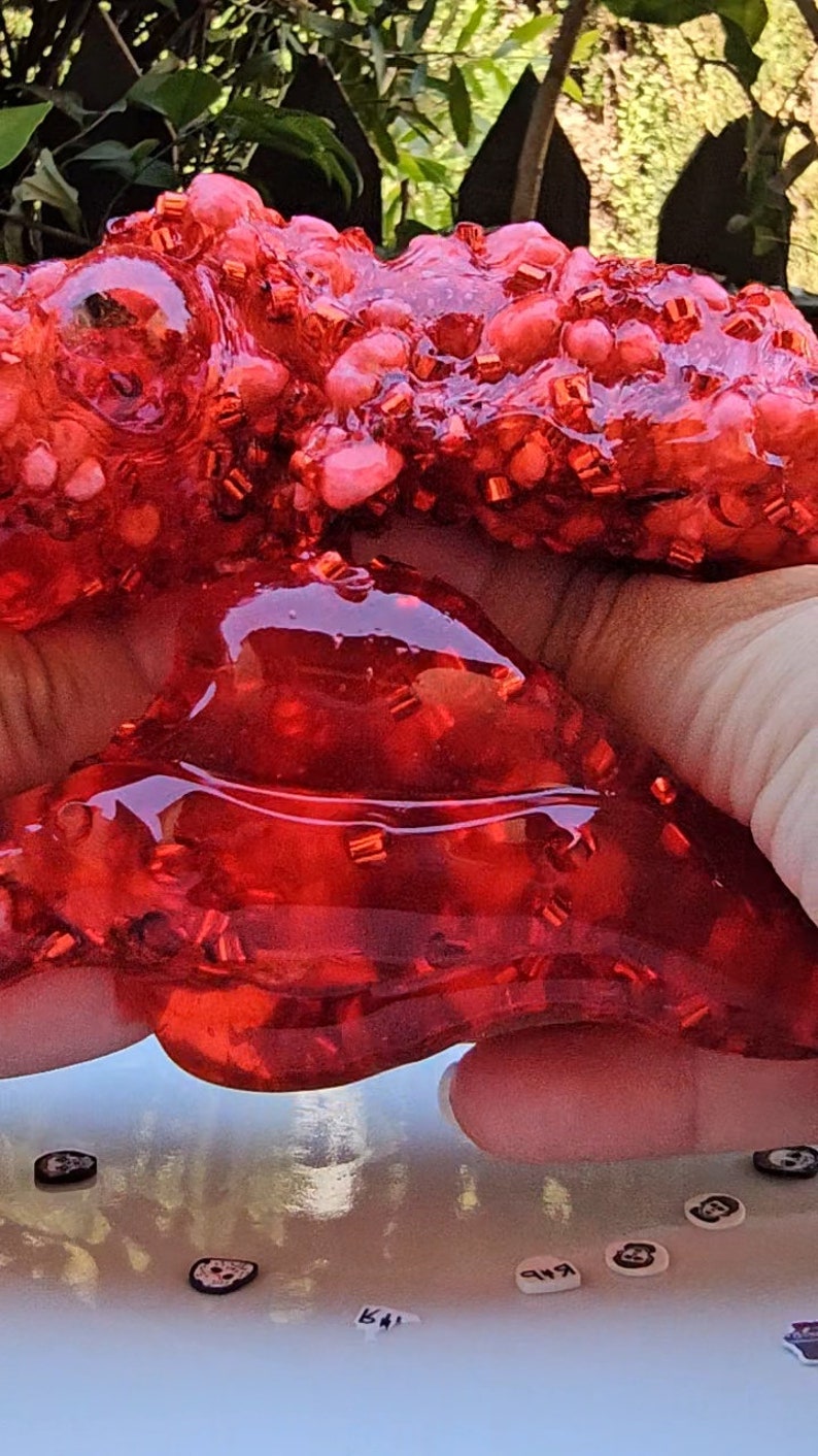 May include: Red slime with red glitter, held in a hand. The slime is very thick and gooey.