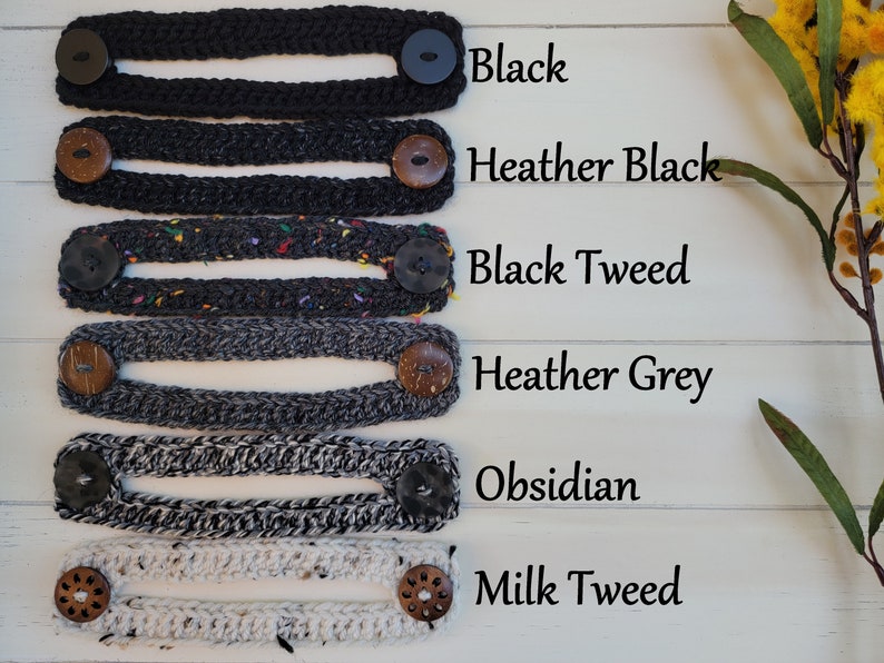 Op de afbeelding: Zes gebreide maskerverlengers in verschillende kleuren en patronen, waaronder zwart, grijs-zwart, zwart tweed, grijs-grijs, obsidiaan en melk-tweed. Elke verlenging heeft aan beide uiteinden twee knopen.