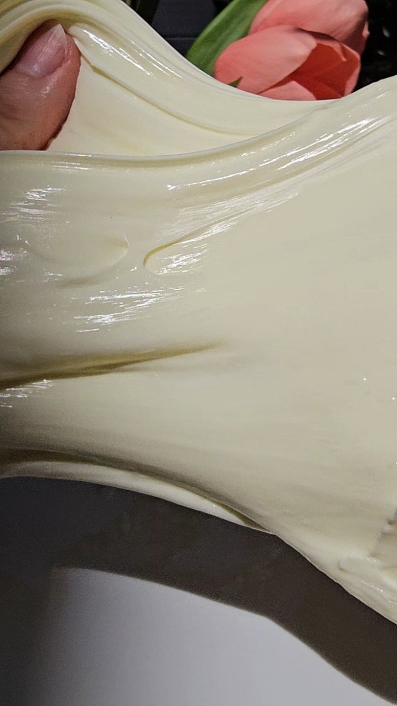 May include: Close-up of a white, creamy slime being stretched and pulled. The slime is smooth and glossy, with a slightly translucent appearance.