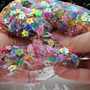 May include: Clear slime with iridescent flower-shaped sequins in shades of pink, purple, blue, green, and yellow.