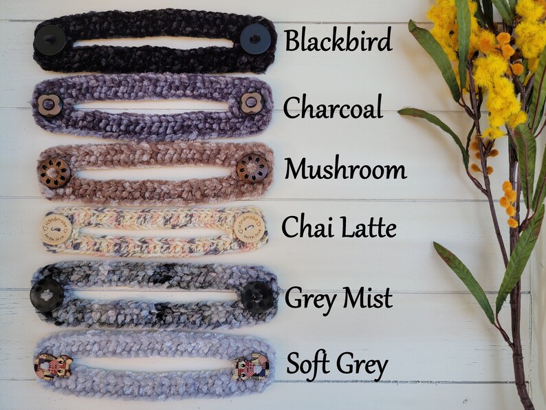 Op de afbeelding: Zes gebreide maskerverlengers in verschillende kleuren, waaronder blackbird, charcoal, mushroom, chai latte, grey mist en soft grey. Elke verlenging heeft twee knopen aan de uiteinden.