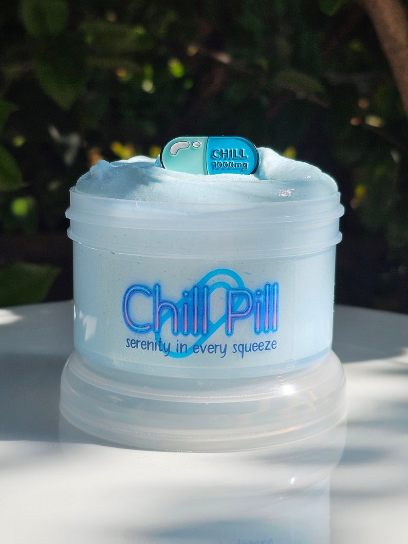 May include: A light blue slime in a clear plastic container with a blue pill charm on top. The container has the words "Chill Pill" and "Serenity in every squeeze" printed on it.