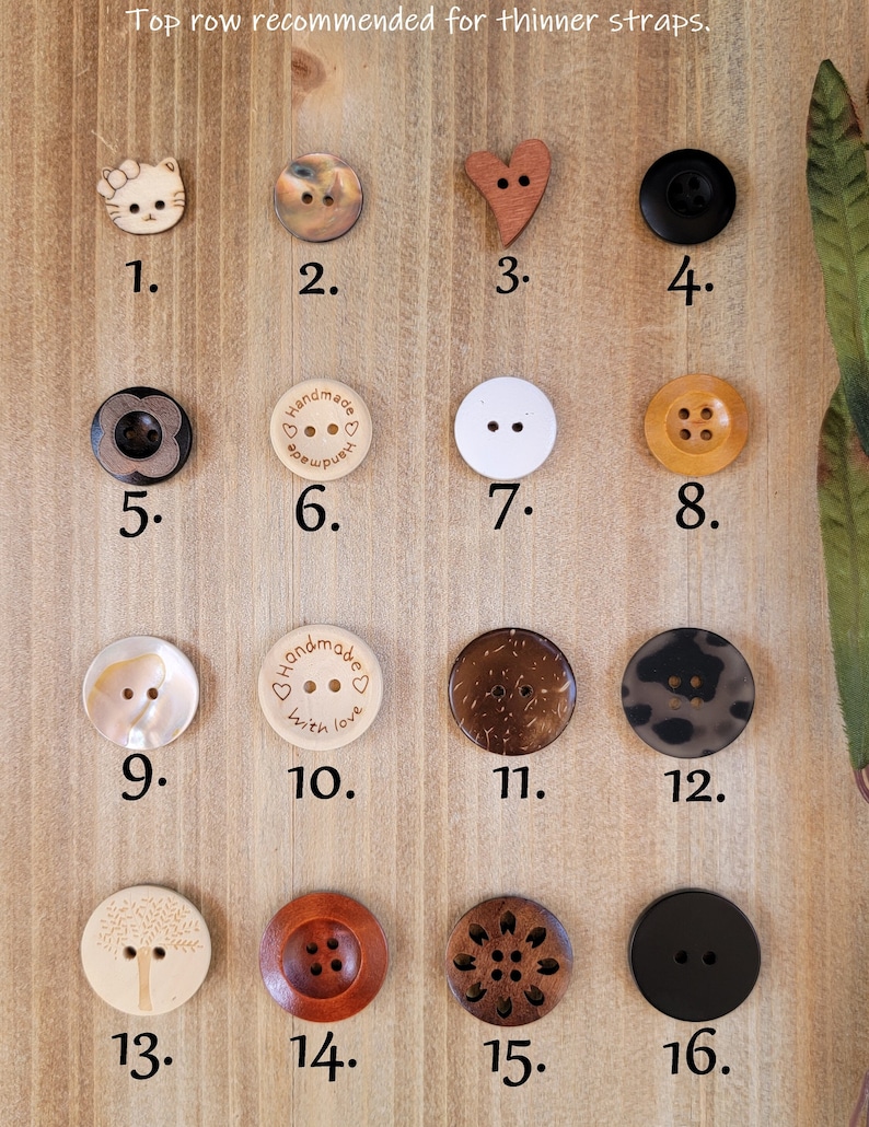 Op de afbeelding: Assortiment van 16 houten knopen in verschillende vormen, kleuren en ontwerpen. De knopen zijn gerangschikt in vier rijen van vier knopen. De bovenste rij is gelabeld "Bovenste rij aanbevolen voor dunnere banden". De knopen omvatten een kat, een hart, een cirkel, een bloem, een cirkel met de woorden "Handmade with love", een boom, een cirkel met vier gaten, een bloem en een cirkel.