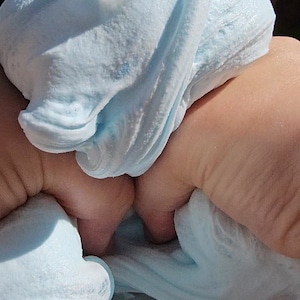 May include: A light blue slime with a clear orb embedded in it. The slime is being held by a hand.