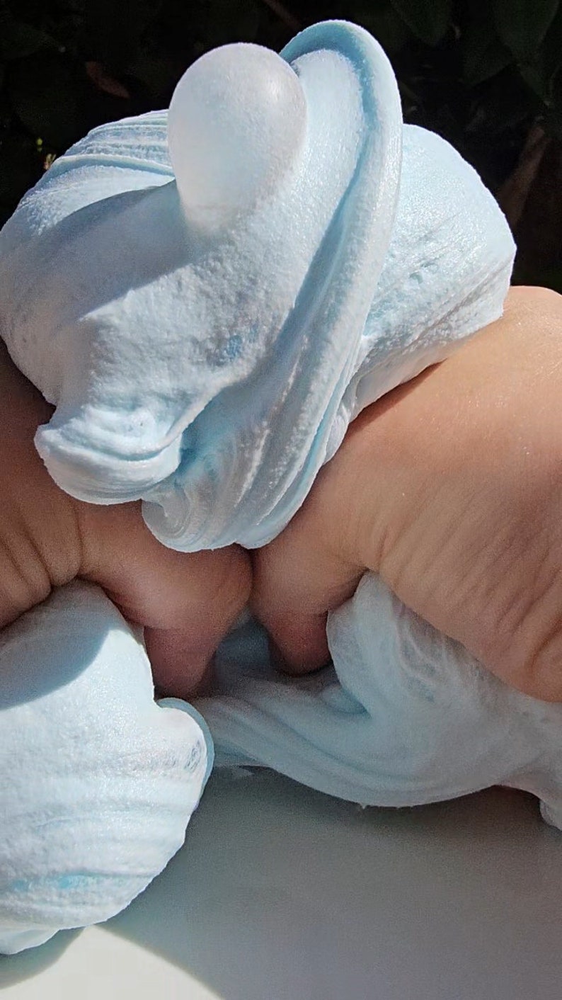 May include: A light blue slime with a clear orb embedded in it. The slime is being held by a hand.