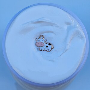 May include: White slime with a gold cow charm. The cow is white with black spots and has a pink nose and hooves.