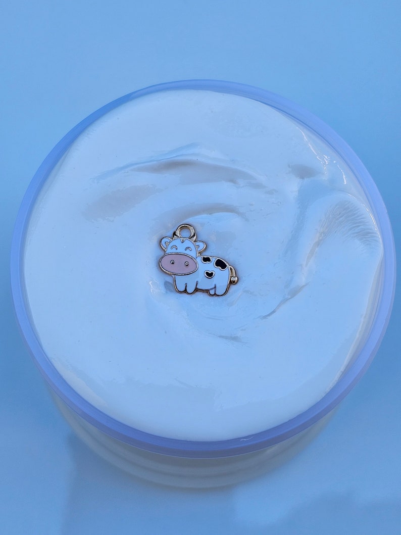May include: White slime with a gold cow charm. The cow is white with black spots and has a pink nose and hooves.