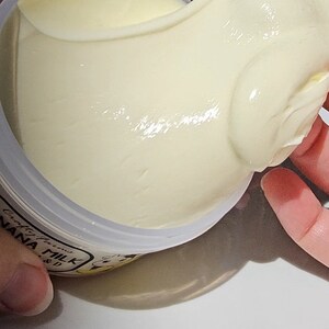 May include: A white jar of banana milk face cream with the text "crafted with love, banana milk" on the label. The cream is being scooped out of the jar with a finger.
