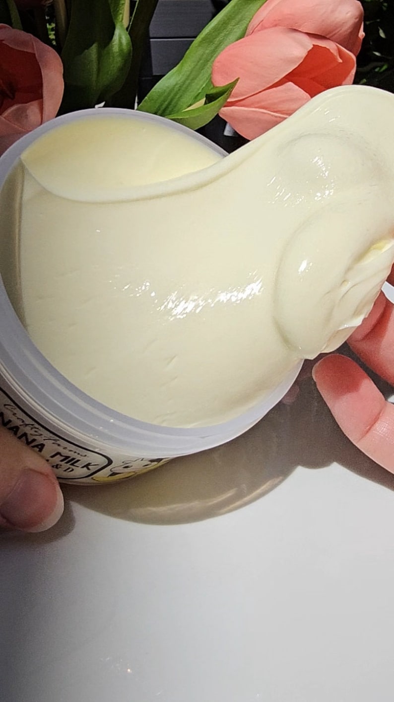 May include: A white jar of banana milk face cream with the text "crafted with love, banana milk" on the label. The cream is being scooped out of the jar with a finger.