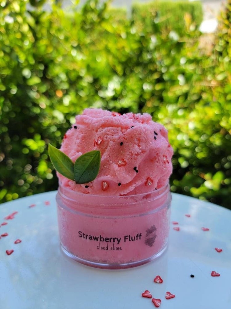 Peut inclure: Un pot transparent de slime nuage de fraise rose avec des p&eacute;pites noires et rouges. Le pot est &eacute;tiquet&eacute; "Strawberry Fluff cloud slime".