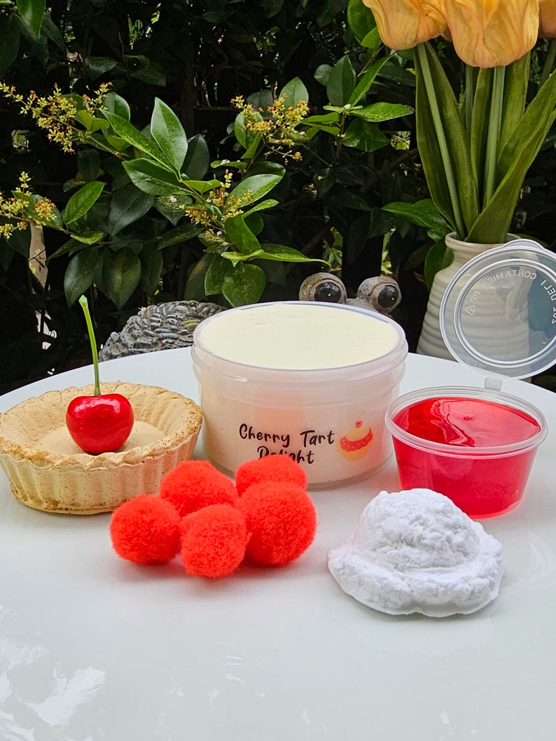 May include: A white jar of cherry tart delight slime, a red cherry tart, red pom poms, a white fluffy slime, and a red jelly slime in a clear plastic container.