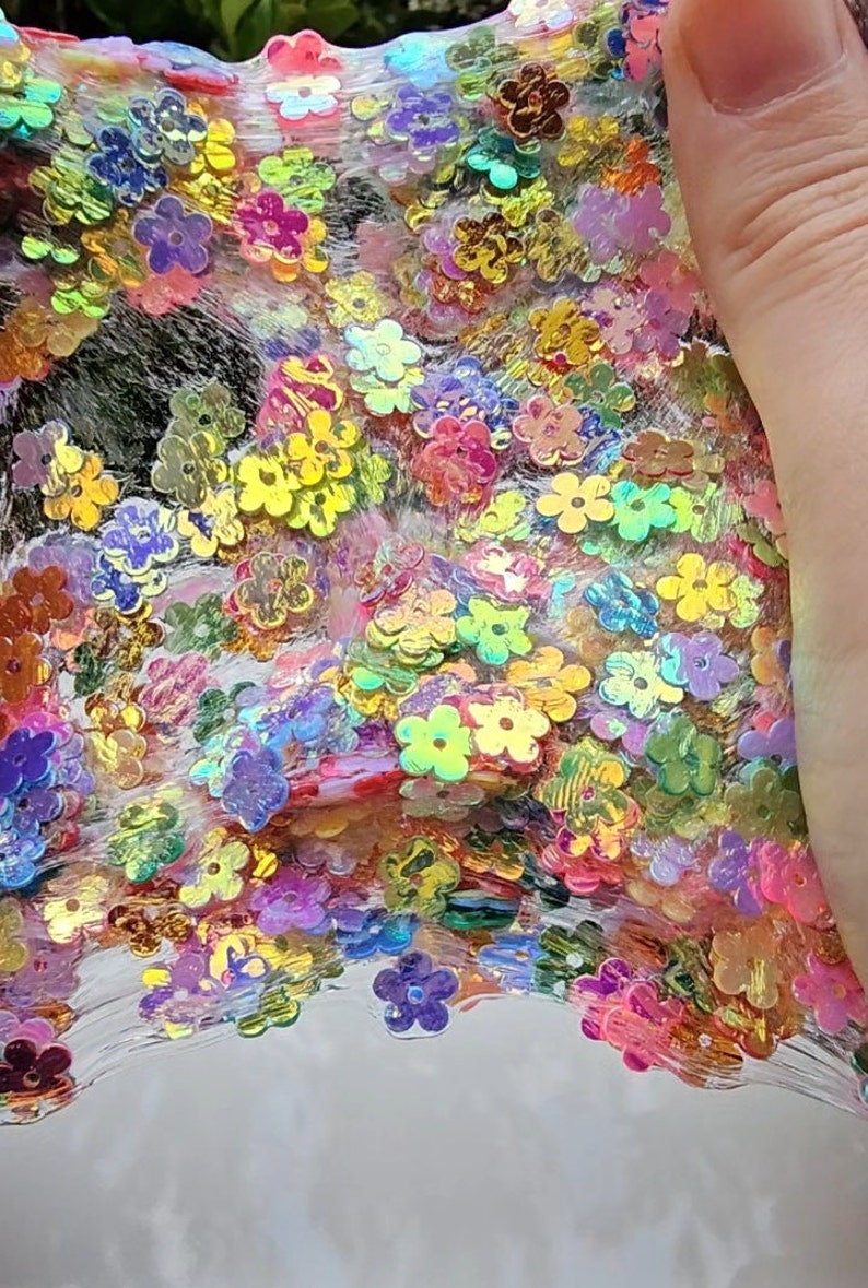 May include: Clear slime with iridescent flower-shaped glitter. The slime is thick and gooey, and the glitter is scattered throughout.
