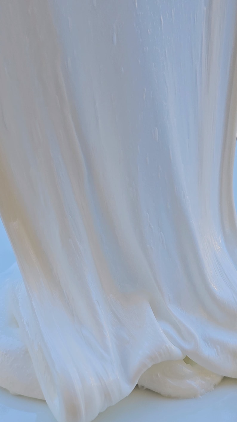 May include: Close-up of white slime with a smooth, glossy texture. The slime is draped over itself, creating folds and ripples.