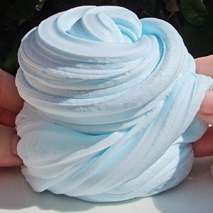 May include: A close-up of light blue slime, a popular sensory toy, with a smooth, soft texture. The slime is folded and twisted into a swirl pattern.