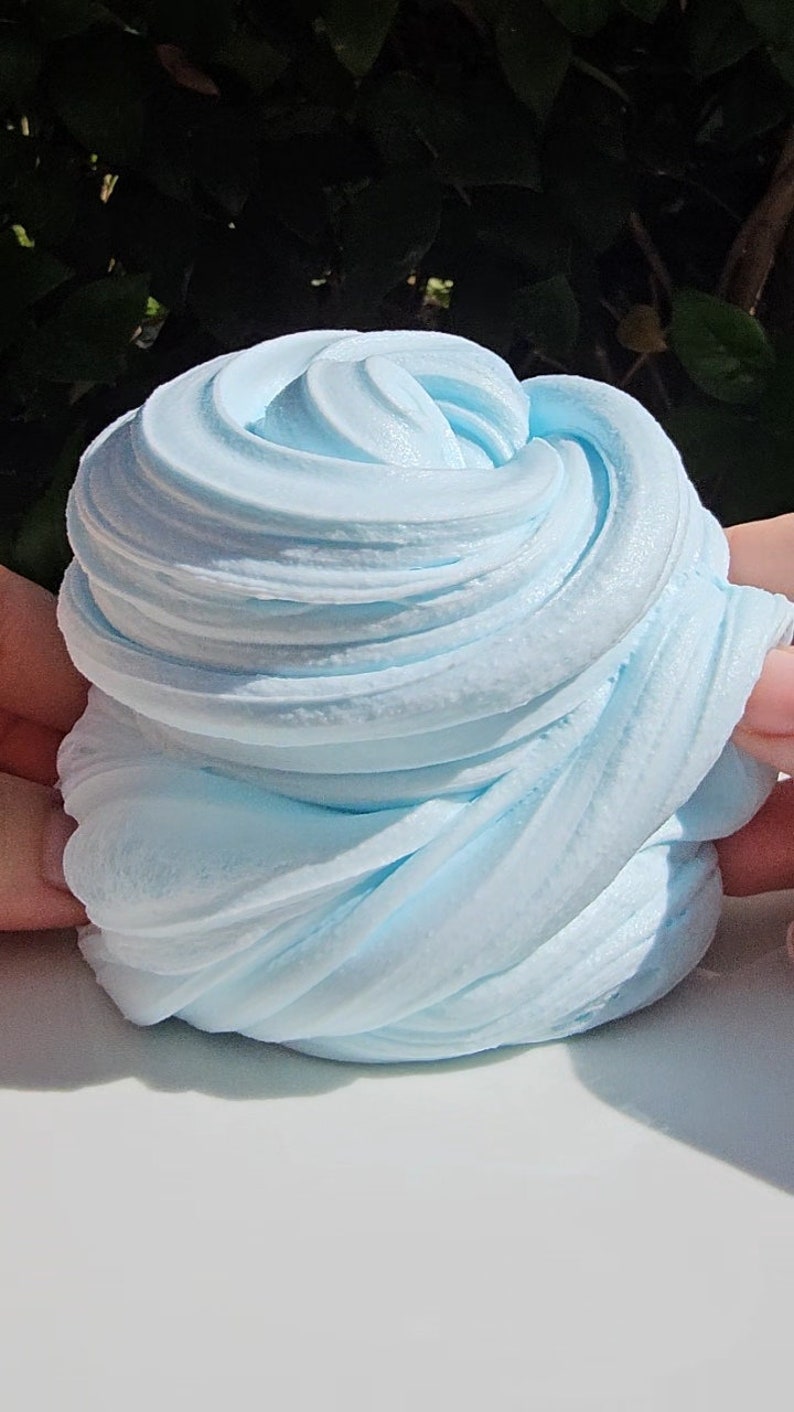 May include: A close-up of light blue slime, a popular sensory toy, with a smooth, soft texture. The slime is folded and twisted into a swirl pattern.
