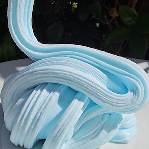May include: A close-up of light blue slime, a popular children's toy, on a white surface. The slime is soft and stretchy, and it has a smooth, glossy finish.