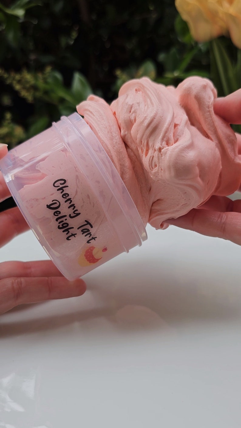 May include: A pink slime with a swirl pattern in a clear plastic container with a label that reads "Cherry Tart Delight".