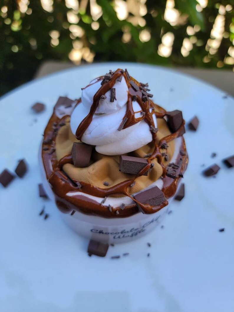 以下が含まれることがあります： チョコレートチップワッフルカップにホイップクリーム、チョコレートソース、チョコレートチップがトッピングされています。カップには「チョコレートチップワッフル」とラベルが貼られています。