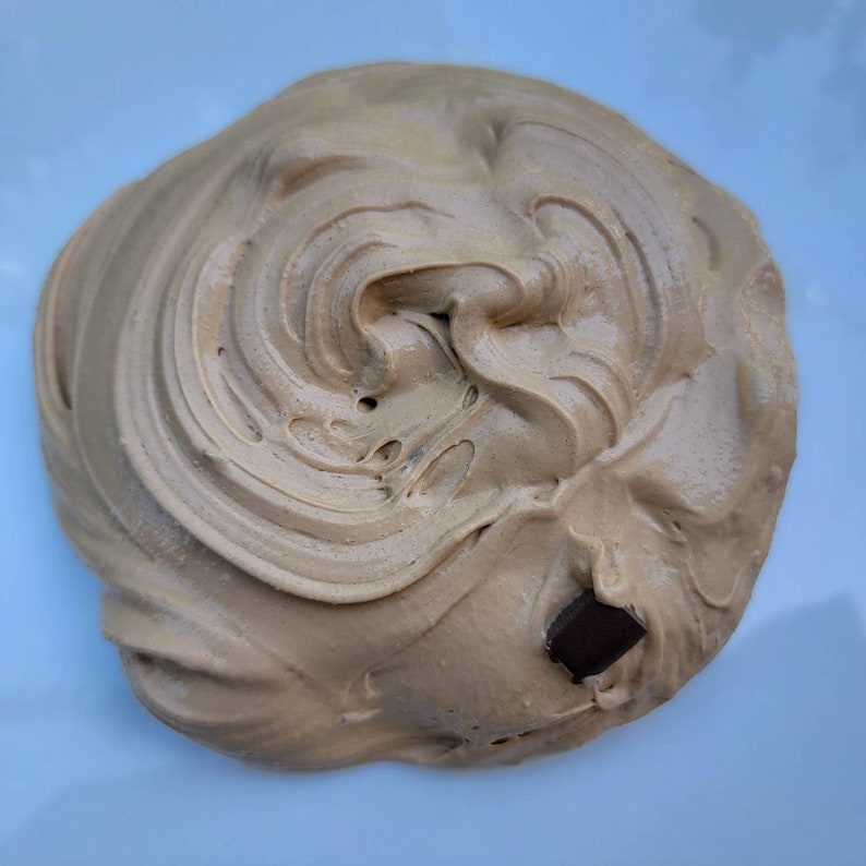 以下が含まれることがあります： 渦巻き状の茶色のスライムのクローズアップ。小さなチョコレートが埋め込まれています。
