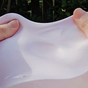 K&ouml;nnte beinhalten: Nahaufnahme von einem hellrosa Schleim, der gedehnt und gezogen wird. Der Schleim ist glatt und gl&auml;nzend und hat eine leicht durchscheinende Optik.