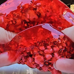 May include: Red slime with red and gold glitter inside. The slime is being held in two hands.