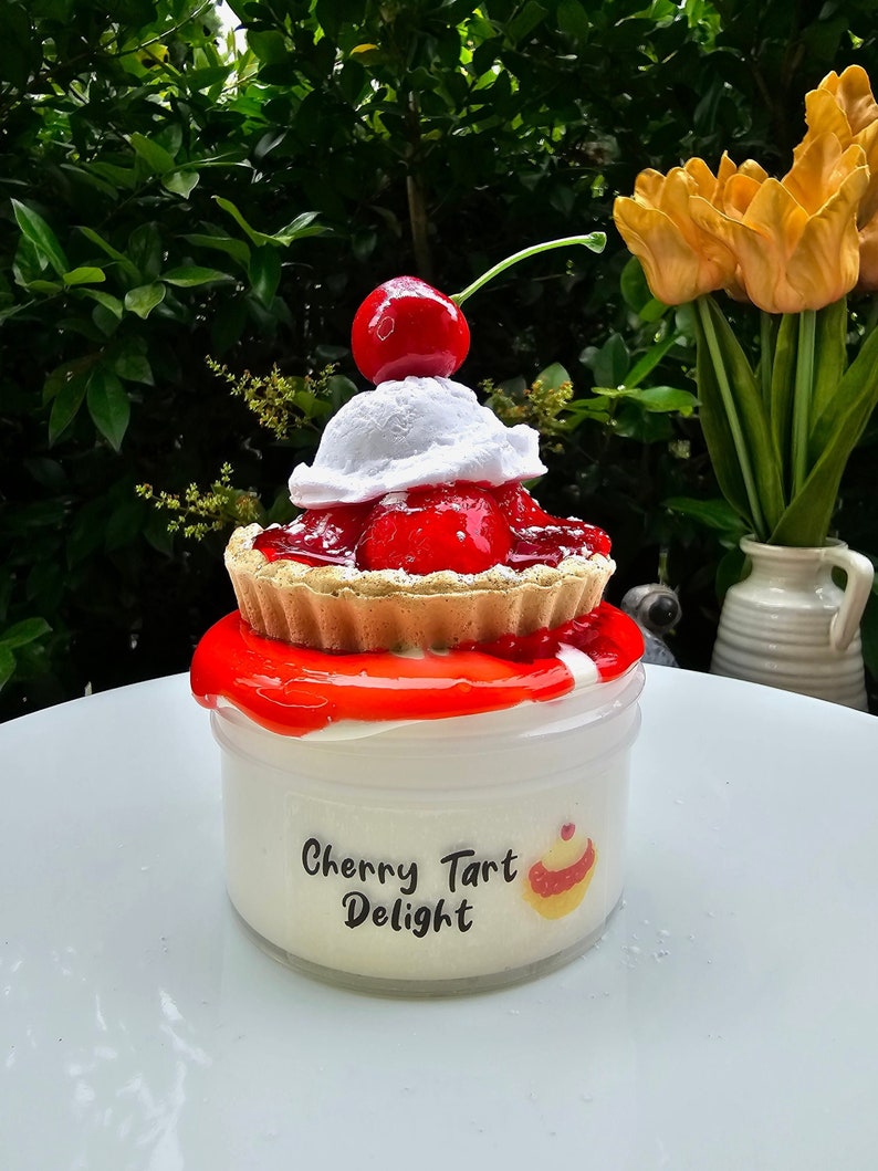 May include: A white jar with red cherry topping and a white whipped cream topping. The jar has a label that says "Cherry Tart Delight".