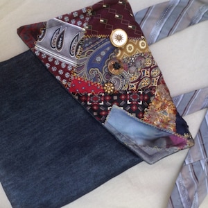Può includere: Una borsa tote in denim con un design a patchwork realizzato con cravatte riutilizzate. Il patchwork include vari colori e motivi, tra cui disegni paisley, geometrici e a righe. La borsa ha una lunga tracolla realizzata con una cravatta a righe.