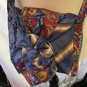 Può includere: Una borsa in tessuto blu e marrone con un motivo floreale. La borsa è realizzata con tessuto riciclato e ha un design unico.