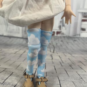 May include: A pair of blue and white knee-high socks with a cloud pattern. The socks are worn by a doll with brown shoes.