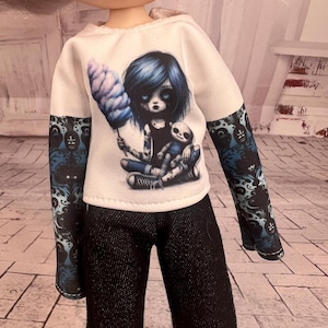 May include: A doll wearing a white hoodie with a graphic of a blue-haired figure holding cotton candy and a doll. The sleeves are patterned with blue and black designs. The doll is also wearing black pants.