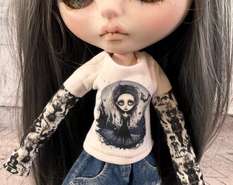 Könnte beinhalten: Eine Custom-Puppe mit grauem Haar, die ein weißes T-Shirt mit einer gotischen Illustration und eine blaue Jeans trägt. Die Arme der Puppe haben schwarz-weiße Tattoo-Ärmel. Die Puppe hat große Augen und einen blassen Teint.