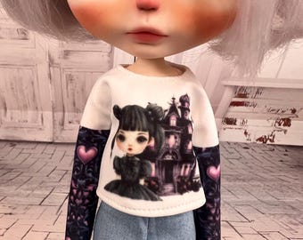 Könnte beinhalten: Eine Puppe trägt ein weißes Langarmshirt mit einem Aufdruck eines Mädchens und eines Spukhauses. Die Ärmel sind dunkel mit rosa Herzen. Die Puppe trägt auch eine blaue Jeans.