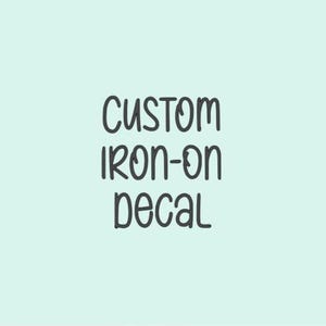 May include: A light blue background with the words "CUSTOM IRON-ON DECAL" in a dark gray, handwritten-style font. The text is vertically centered in the image.
