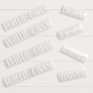 May include: A collection of white vinyl adhesive decals featuring custom text. Four decals display the phrase PHILLIE GIRLS, while four individual decals feature the names BOHM, TURNER, WHEELER, and HARPER in a clean, sans-serif font style.