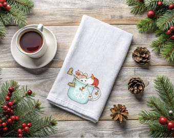 以下が含まれることがあります： クリスマスデコレーションに囲まれた、ティーカップの中のネズミの漫画イラストが描かれた白いティータオル。左にはソーサーに載った紅茶のカップがあります。松ぼっくりと赤い実のついた常緑樹の枝が、お祝いのシーンを完成させています。