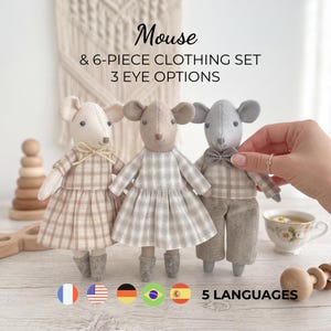 Puede incluir: Tres muñecos de ratón de peluche con detalles cosidos. El ratón de la izquierda lleva un vestido de cuadros beige con un lazo. El del centro lleva un vestido de cuadros grises. El de la derecha lleva camisa y pantalón de cuadros grises con pajarita. Texto: Mouse & 6-PIECE CLOTHING SET 3 EYE OPTIONS.