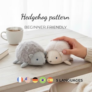Puede incluir: Dos juguetes de erizo de peluche, uno gris y otro blanco, sobre una superficie de madera clara. El erizo gris tiene cara y orejas azules, mientras que el blanco tiene cara color crema. El texto superior dice "Hedgehog pattern BEGINNER FRIENDLY."