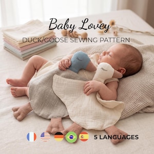 May include: A baby lovey duck and goose sewing pattern featuring two soft fabric toys with embroidered eyes. The text reads Baby Lovey DUCK/GOOSE SEWING PATTERN and 5 LANGUAGES. The toys are cream and blue, shown with a stack of folded fabric.