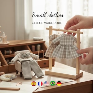 Op de afbeelding: Een miniatuur 7-delige garderobeset met kleine kleding. De set bevat een miniatuur houten kledingrek met twee geruite jurken, een trui met een strik en een broek. De tekst "Small clothes" en "7-PIECE WARDROBE" zijn zichtbaar.