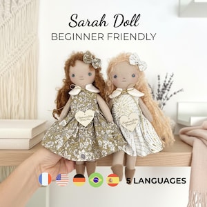 Puede incluir: Dos muñecas de tela llamadas Sarah Doll, una con cabello castaño y vestido floral, la otra con cabello rubio y vestido con estampado dorado. Ambas llevan cuellos blancos, lazos y etiquetas en forma de corazón que dicen Celebrate Who You Are. Texto: Sarah Doll BEGINNER FRIENDLY 5 LANGUAGES.