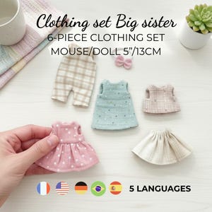Peut inclure: Un ensemble de six vêtements pour une souris ou une poupée, comprenant une robe rose à pois, un haut bleu clair à pois, une jupe beige et d'autres pièces. Conçu pour une poupée de 13 cm. Le texte "Clothing set Big sister" est visible.
