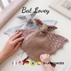 May include: Two bat lovey security blankets with textured plush bodies and patterned fabric wings. One is grey with a blue grid pattern, and the other is brown with a white floral print. The text Bat Lovey is displayed at the top of the image.