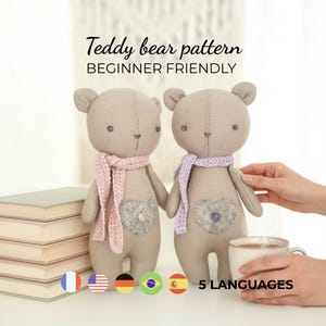 May include: Two beige teddy bears with pink and purple scarves, heart-shaped patches, and blue eyes. The text "Teddy bear pattern BEGINNER FRIENDLY" is displayed above the bears. A cup of coffee and a stack of books are also visible.
