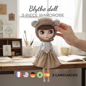 May include: A Blythe doll wearing a 3-piece wardrobe, including a brown bear-eared hat, a floral patterned top, and a tan skirt. The doll is on a wooden surface. The image includes the text "Blythe doll 3-PIECE WARDROBE".