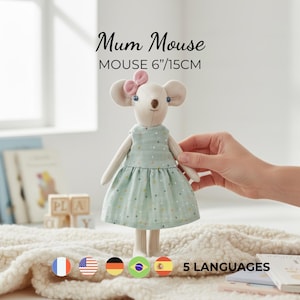 May include: A plush mouse toy named Mum Mouse, measuring 6 inches tall. The mouse has cream-colored fur, a small pink bow on its head, and blue eyes. It wears a light green sleeveless dress with a subtle multicolored polka dot pattern.